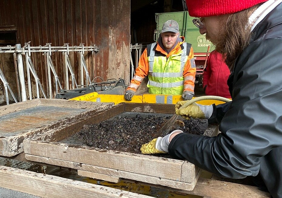 Bodenproben werden auf einem großen Sieb auf kleine Fundstücke untersucht