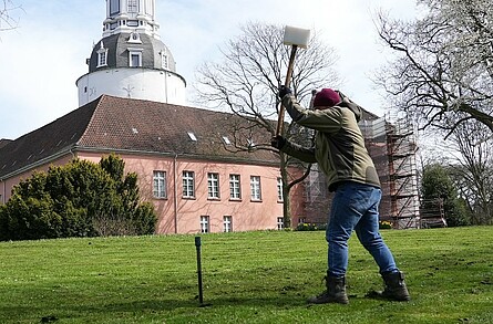 Ein Mann schlägt mit einem Bohrhammer auf einen Erdbohrer vor der Kulisse des Schloßes